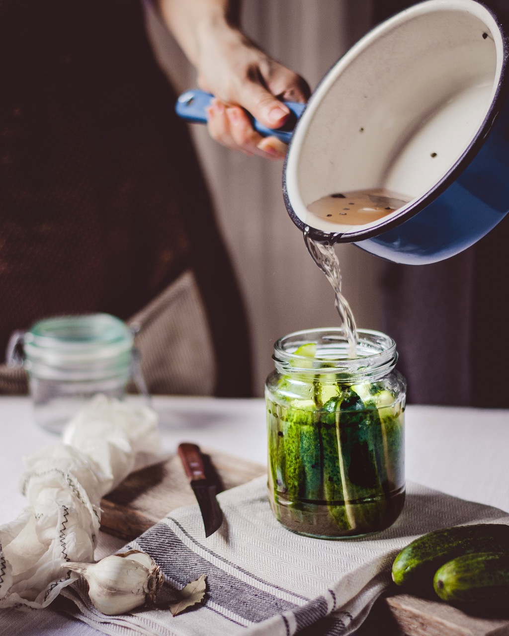 Een hand schenkt water met zout bij komkommers